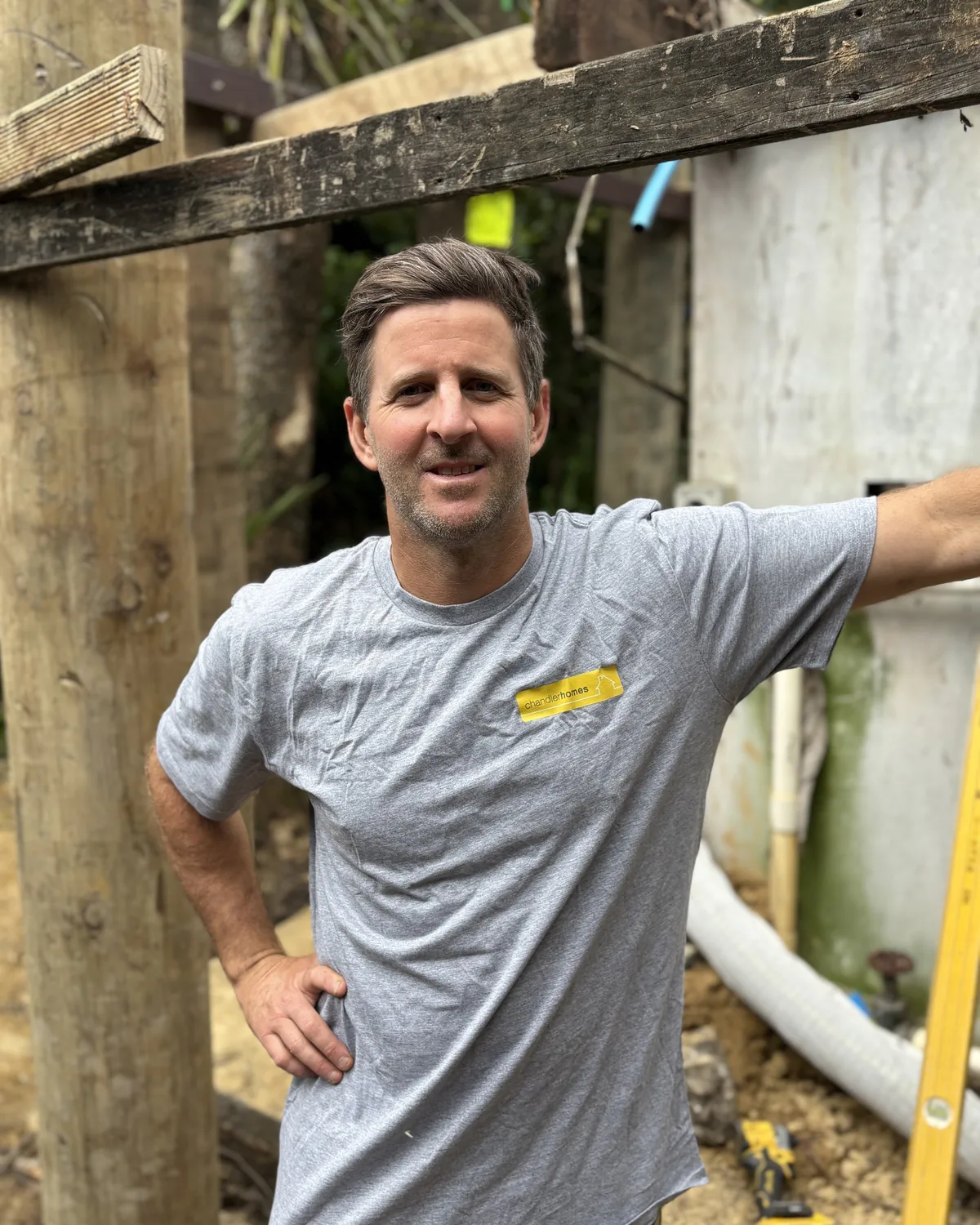 Adam Chandler on site in a grey Chandler Homes t-shirt, standing beside timber posts
