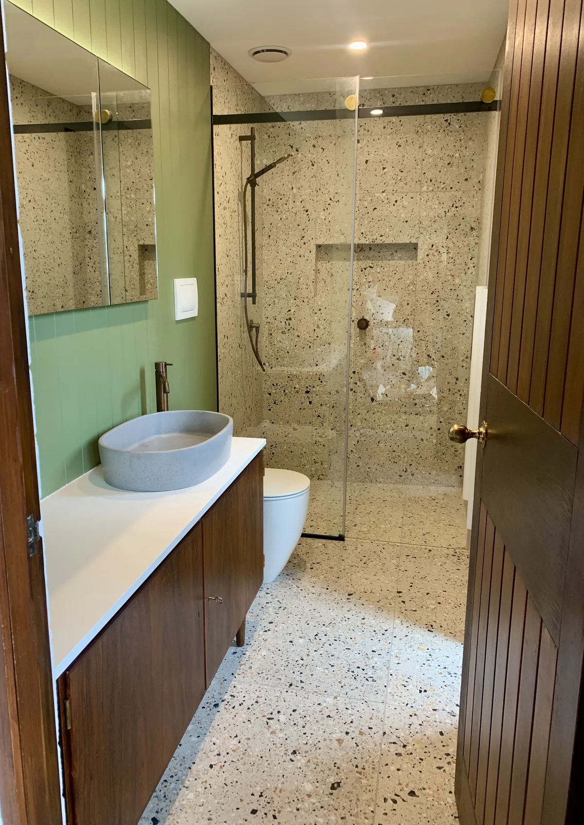 Bathroom with green panelled walls, terrazzo tiles, a timber vanity and a frameless glass shower