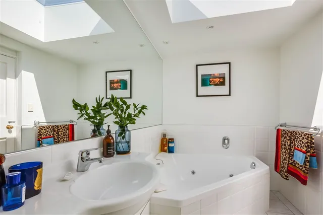 Before: white tiled bathroom with a corner spa bath, a white vanity and two skylights