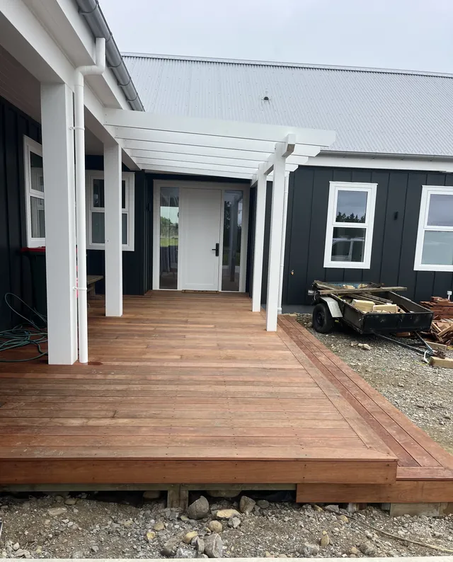 New timber deck with a white pergola at the front door of a dark clad house
