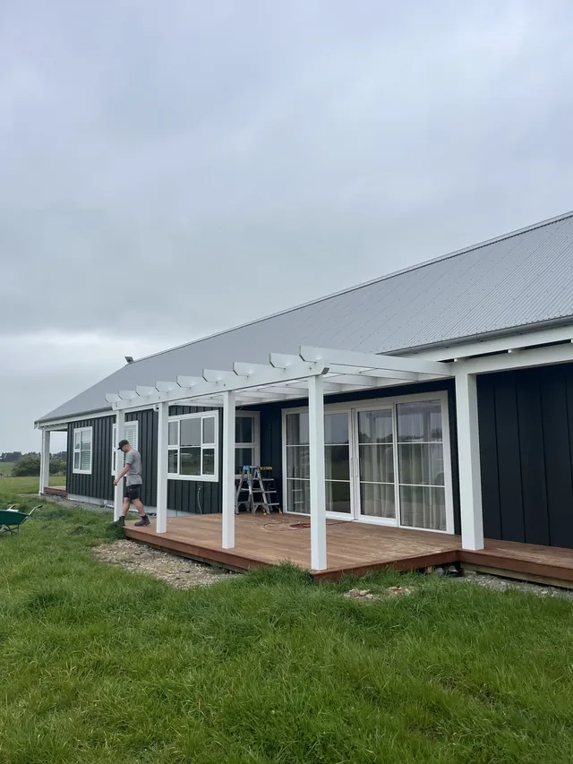 Long timber deck and white pergola along a dark clad house