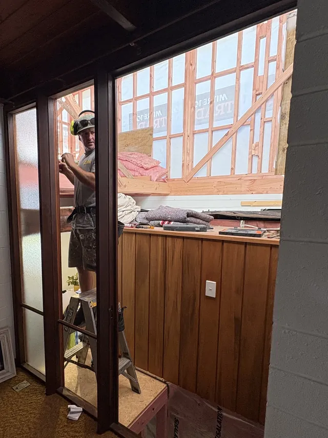 Builder fixing framing for the new level, seen through a doorway from inside the existing house