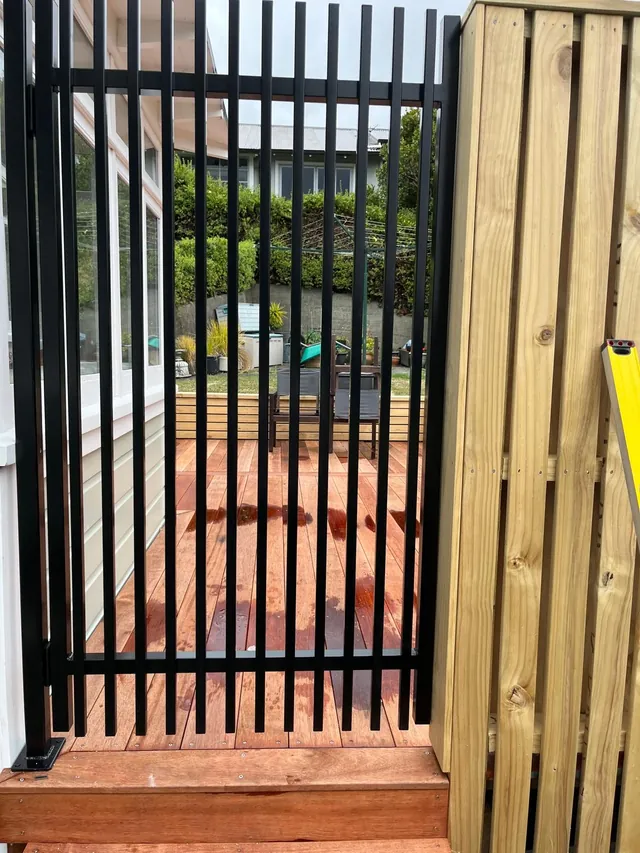 Black slatted gate next to a vertical timber fence