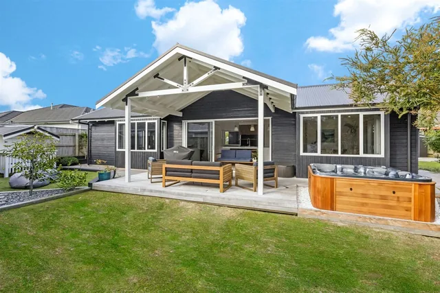 Covered outdoor area with exposed white trusses over a timber deck, beside a lawn