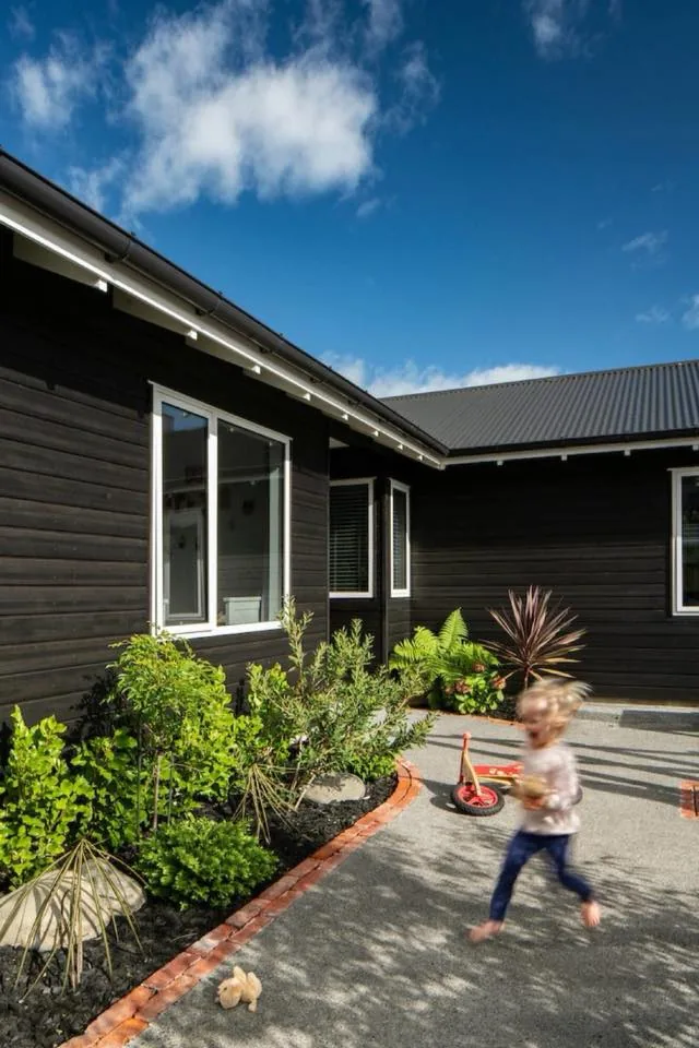Front path and planting beside dark weatherboard cladding, with a child running past