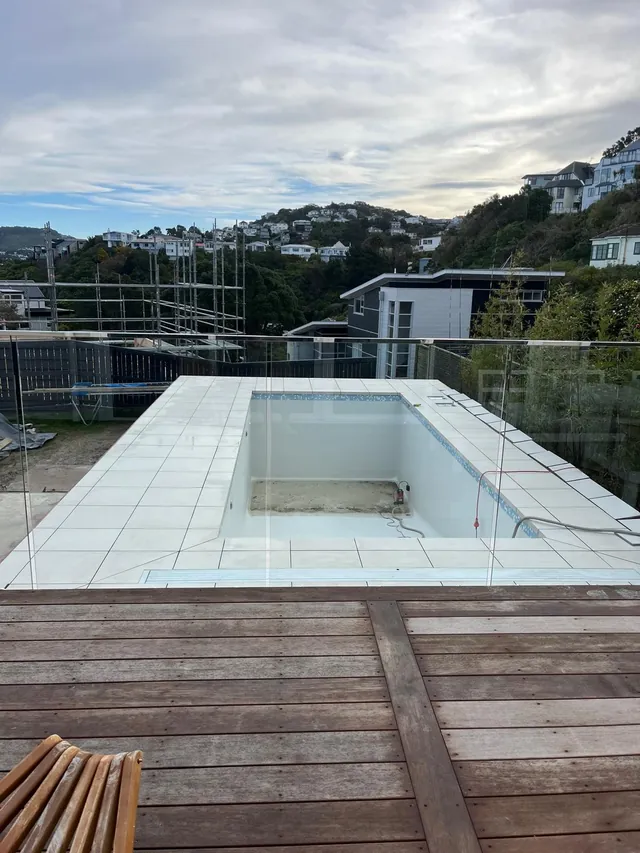 Tiled pool seen from a new timber deck, with glass fencing