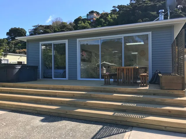 Single-storey house with pale blue weatherboards and two sets of glass doors opening onto a timber deck with wide timber steps and outdoor seating