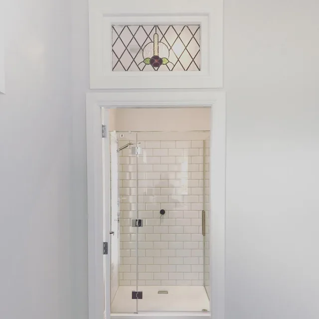 En-suite doorway with a leadlight stained glass window above it, looking into a white tiled shower with a frameless glass door