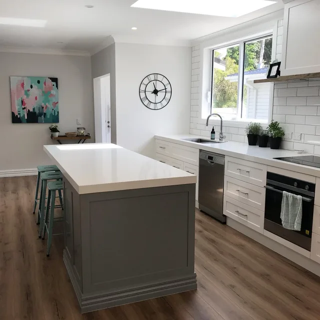 White kitchen with a grey island bench and stools, subway tile splashback, a window over the sink and a skylight above