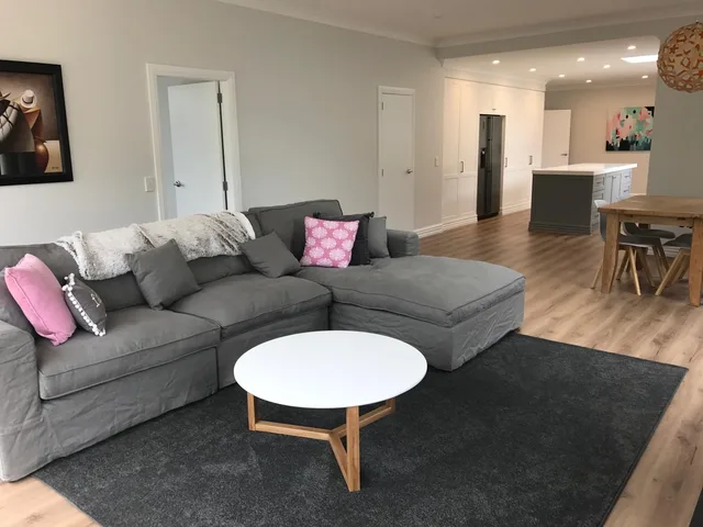 Open-plan living area with a grey corner sofa, round coffee table, downlights and a skylight, leading through to a dining table and kitchen