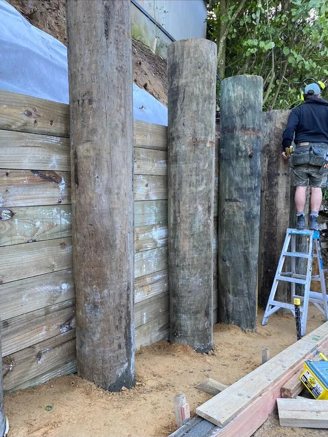 Builder on a ladder fixing timber lagging behind tall retaining poles