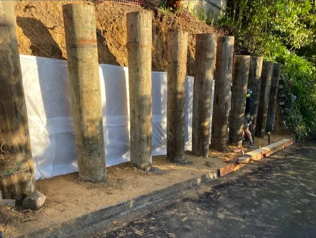 Timber poles in place in front of a cut bank lined with white cloth