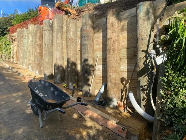 Finished timber pole retaining wall with lagging, beside a path