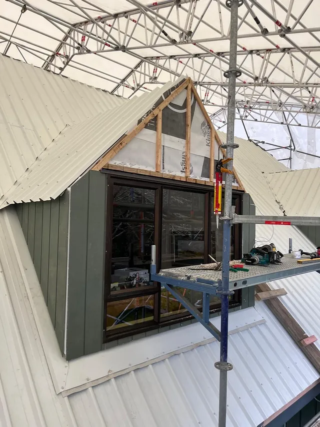 Dormer with green vertical cladding and new roofing iron around it, beside scaffolding