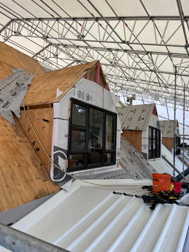 Dormer window framed and wrapped in building paper on a plywood roof under a scaffold cover