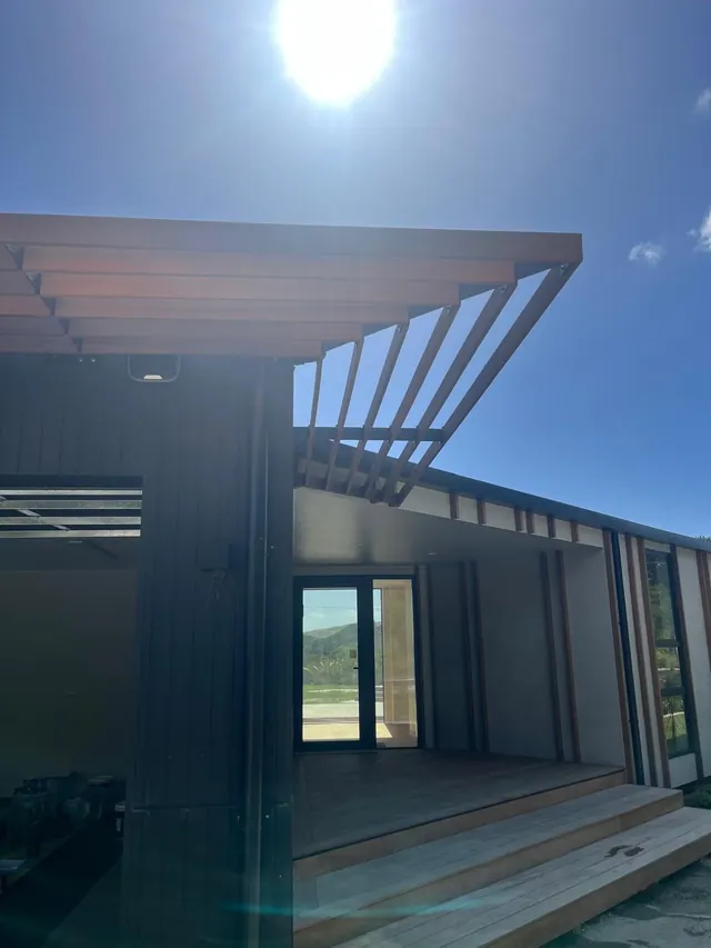 Angled timber battens forming a screen over the covered entry deck of a dark clad house